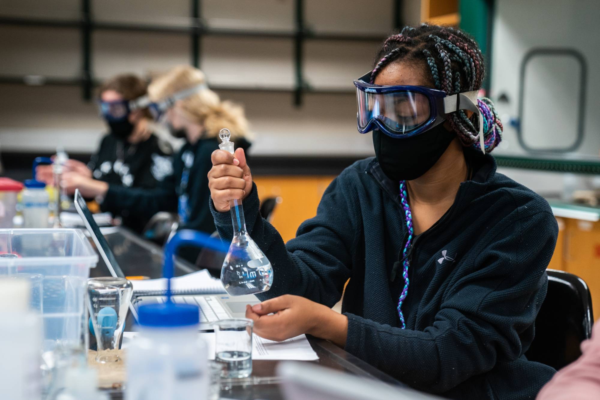Student works in Chemistry lab in full PPE and is holding a breaker of clear liquid